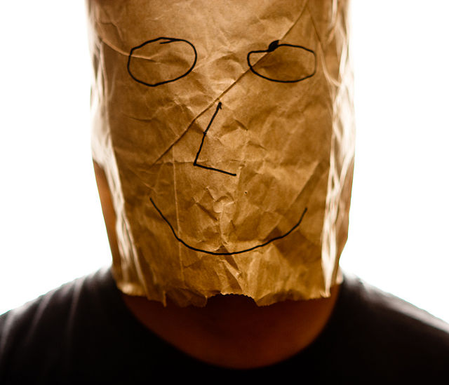 A person with a bag over their head. A smiley face is drawn on the bag.